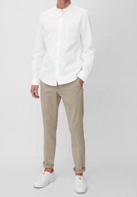 Vit långärmad skjorta med ståkrage, i kombination med beige chinos och vita sneakers med orangea accenter. Enkelt och modernt design.