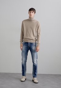 Maglione a collo alto beige chiaro, jeans slim-fit blu sbiaditi e scarpe slip-on beige. Design semplice con minima texture e dettagli.