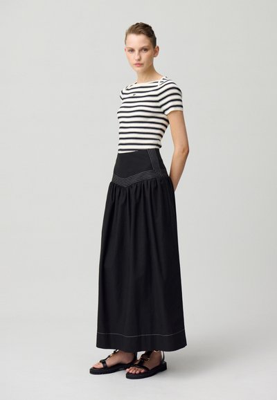 Haut ajusté rayé noir et blanc, associé à une jupe noire taille haute avec une texture froncée et des détails de couture blanche. Sandales noires.