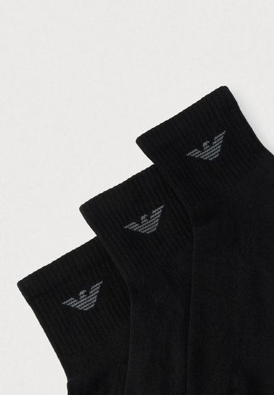 Czarne bawełniane skarpetki o prążkowanej fakturze z szarym emblematem na mankiecie, starannie ułożone w rzędzie.