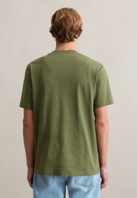 Oliwkowo-zielona koszulka z krótkim rękawem i okrągłym dekoltem, wykonana z miękkiej bawełnianej tkaniny; prosty, luźny krój bez zdobień.