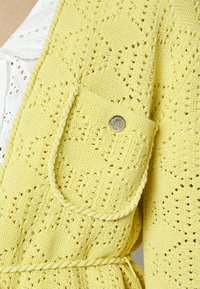 Żółty dziergany kardigan z teksturowanym wzorem, przedni�ą kieszenią z srebrnym guzikiem oraz paskiem do wiązania.