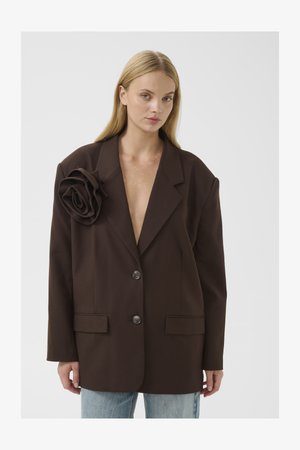 Barna, oversized blézer, nagy textilrózsa díszítéssel a bal vállon. Két elülső gombbal és rakott zsebekkel rendelkezik.