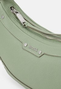 Borsa a mano in pelle verde con superficie texture, accessori in argento, logo del marchio impresso e chiusura con zip. Presenta un design curvo e cuciture in contrasto.