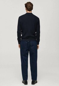 Navy ribbed knit sweater with a round neck, paired with dark blue straight-leg jeans. Shoes are black with a smooth finish.