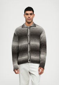 Sweter z dzianiny w odcieniach szarości w gradiencie. Posiada kołnierz, pełne zapięcie na guziki z przodu oraz prążkowane mankiety. Miękka tekstura i luźny krój.