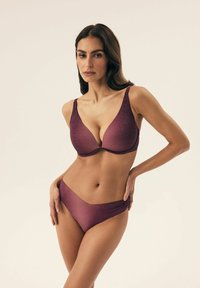Zestaw bikini w głębokim purpurze z delikatnym połyskiem. Biustonosz ma profilowane miseczki i szerokie ramiączka, podczas gdy dolna część bikini ma niską talię i gładką teksturę.