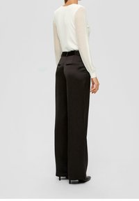 Pantalon noir à jambes larges avec poches arrière et taille ajustée, assorti à un haut de couleur claire avec des manches côtelées et transparentes.