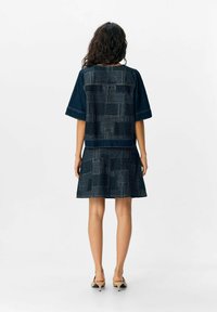 Jeansklänningsset i mörkblått med ett mönstrat jacka. Har korta ärmar, en figurnära topp och en utsvängd kjol med texturerade detaljer.