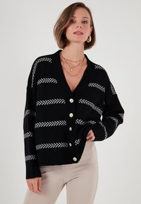 Svart cardigan med vita herringbone-ränder, V-ringning, långa ärmar och silverknappar fram. Designad med en avslappnad passform.