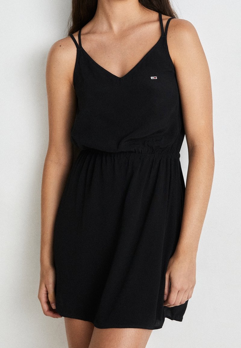 Czarna sukienka z dekoltem w serek, cienkimi ramiączkami i elastycznym pasem. Wykonana z lekkiego materiału o prostym, zwiewnym fasonie.