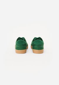 Green suede sneakers with a rounded toe, rubber gum sole, and subtle stitching details. Rear view shows cushioned collar design.