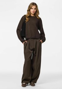 Maglione marrone lavorato a maglia abbinato a pantaloni marroni a vita alta e ampi. Colore d'accento: calzature beige. Design casual e testurizzato.