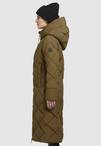 Long, olive green puffer coat with a hood, diamond quilted pattern, side pockets, and a logo patch on the left sleeve. Black beanie worn.