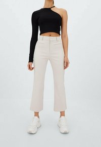 Black cropped top with one long sleeve, paired with beige flared trousers and white sneakers. Smooth fabric, minimalistic design.