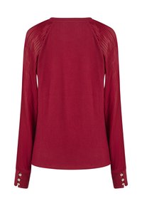 Rotes Langarmshirt mit einem einfarbigen Körper und durchsichtigen, gerippten Ärmeln. Verfügt über Knopfdetails an den Bündchen. Insgesamt glatte Textur.
