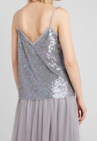 Top argentato con paillettes e design a V sulla schiena, dotato di sottili spalline regolabili e bordo arricciato, abbinato a una gonna in tulle grigio trasparente.