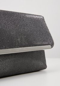 Černá texturovaná kabelka na příležitosti s geometrickým vzorem, stříbrnými kovovými prvky a elegantním designem. Kabelka má klopový uzávěr.