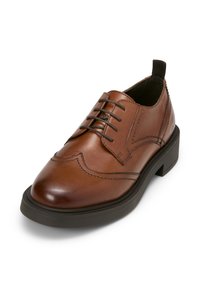 Chaussure habillée en cuir marron avec un bout arrondi, six œillets, des coutures décoratives et une semelle en caoutchouc noir. Dispose d'une languette à l'arrière.