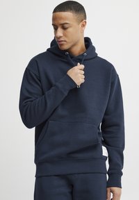 Sudadera azul marino con capucha, bolsillo tipo canguro, puños y cinturilla de canalé. Confeccionada con un tejido suave y texturizado.
