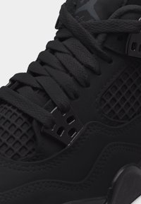 Κοντινό πλάνο μαύρου αθλητικού παπουτσιού που δείχνει κεντημένα κορδόνια, πλευρικό πάνελ από δίχτυ και λεπτομέρεια πλαστικού συγκρατητήρα κορδονιών.