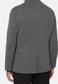 Gray herringbone blazer with a structured collar, single vent at the back, and long sleeves. Textured fabric with a tailored fit.