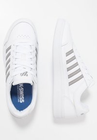 Sneakers bianchi in pelle con strisce grigie. Presentano un design con allacciatura, collo imbottito e suola in gomma testurizzata. Fodera interna blu.