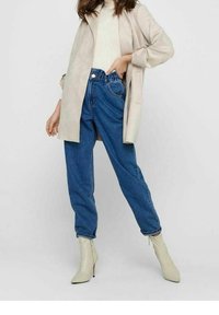 Jeans in denim a vestibilità ampia e vita alta, abbinati a una giacca in suede beige e a un maglione crema. Stivali alla caviglia beige a punta completano l'outfit.
