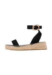 Sandale espadrille en suede noir avec une large sangle à la cheville, des garnitures en or et une semelle en jute. Design à bout ouvert plat.