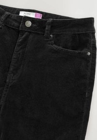 Pantaloni flared din corduroy negru, cu talie înaltă, buzunare frontale, închidere cu buton metalic și model texturat al țesăturii. Eticheta arată "FLARE."