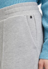 Lichtgrijze sweatpants van zachte stof, met twee zijzakken en een zwart knoopdetail aan de taille. Getextureerde ribbelblauwe mouw.