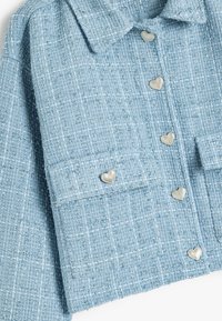 Giacca in tweed blu con una finitura testurizzata, dotata di bottoni argentati a forma di cuore e due tasche frontali.