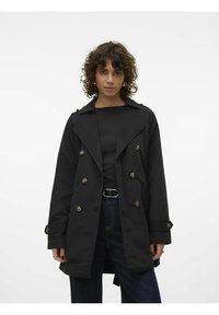 Black double-breasted trench coat with large buttons, wide lapels, and slightly oversized fit, paired with a black top and dark jeans.