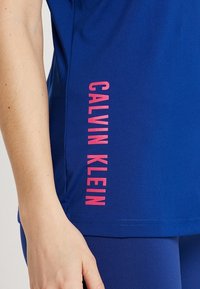 Blauwe korte mouwen top in rekbare stof, met een verticale roze "CALVIN KLEIN" logo aan de linkerkant. Glad materiaal en aangesloten ontwerp.