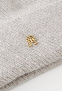 Lichtgrijze gebreide beanie met een zachte textuur, voorzien van een klein gouden logo. De stof heeft een subtiele glans.
