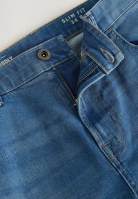 Slim fit modri džins s pilotom na zadrgo, kovinsko gumbno zaklepanje in svetlimi zblanjemi efekti ter podrobnostmi v šivanju. Velikost 34.