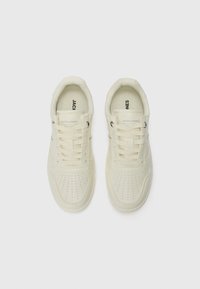 Light cream sneakers with perforated detailing and flat laces, featuring branding on the tongue and side, positioned on a plain background.