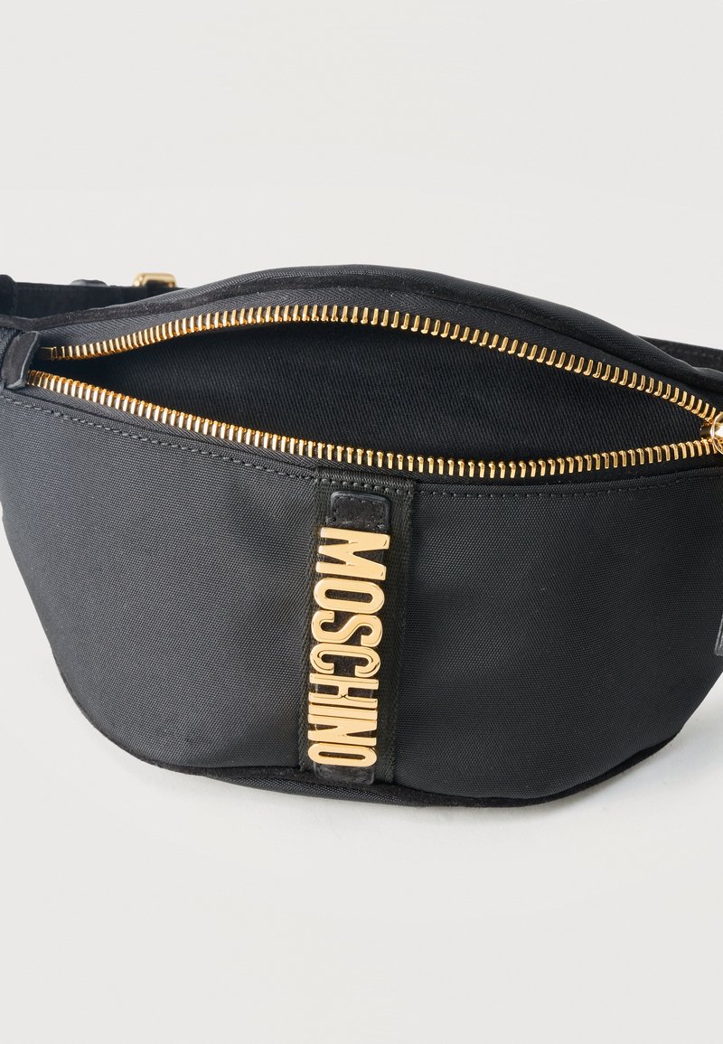Black fabric waist bag with gold zipper and vertical gold Moschino logo on front, shown partially open against white background.