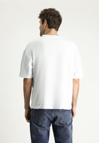 Camiseta blanca de manga corta con corte relajado, cuello redondo y textura suave. Combinada con jeans de denim azul de corte clásico.