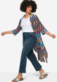 Kimono de colores multicolores con patrones, de mangas largas, que presenta diseños geométricos en azul, naranja y negro, usado sobre una blusa blanca y jeans azules.