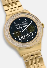 Orologio dorato con bracciale in metallo. Quadrante nero che mostra l'ora e la data, circondato da una lunetta incastonata di cristalli. Accenti floreali in oro.