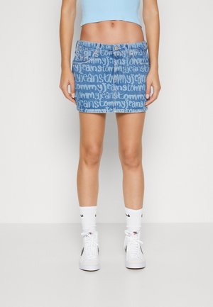 Person iført en blå crop top og en mini cowboynederdel med hvid graffiti tekst, hvide Nike-strømper og hvide Nike højtop-sneakers.