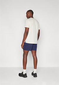 Light beige short-sleeve t-shirt, side slits, paired with navy athletic shorts, and black sneakers with white crew socks. Simple design.