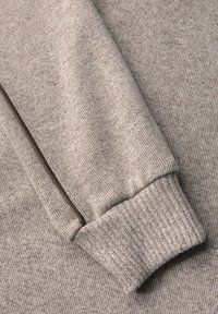 Beige katoenen trui manchet met geribbelde textuur, voorzien van een contrasterende bruine naad langs de rand. Glad, lichtgewicht materiaal.