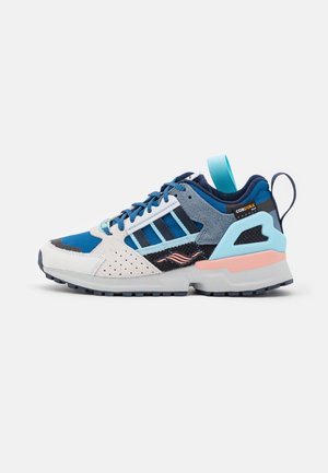 Niski but sportowy z panelami w kolorach niebieskim, białym i szarym, czarne paski, elementy z siateczki, amortyzowana podeszwa i pętle do zakładania na pięcie.