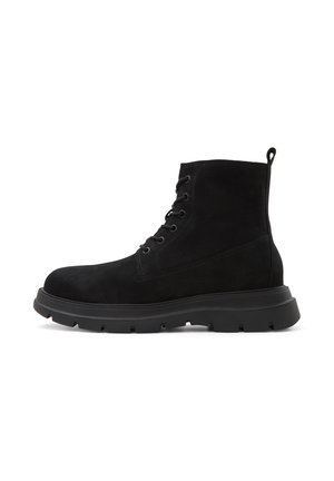 Botas de ante negras hasta el tobillo con punta redonda, detalle de cordones y suela de goma gruesa. Cuenta con una pestaña en el talón para ponerlas y quitarlas fácilmente.