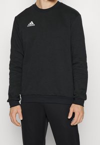 Felpa nera realizzata in tessuto morbido, con collo rotondo, maniche lunghe e logo bianco Adidas sul lato sinistro del petto.