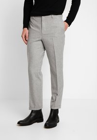 Lichtgrijze broek gemaakt van textuurstof, met een getailleerde pasvorm, rechte snit en gecombineerd met zwarte enkellaarsjes.