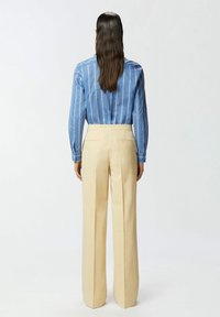 Plava prugasta košulja s dugim rukavima, u kombinaciji s bež visokim širokim hlačama. Glatka tkanina i kroj prilagođen figuri.