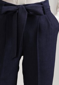 Námořnické modré kalhoty s hladkou texturou, širokým pasem, detailem mašle vpředu a sklady pro zvýšení stylu.